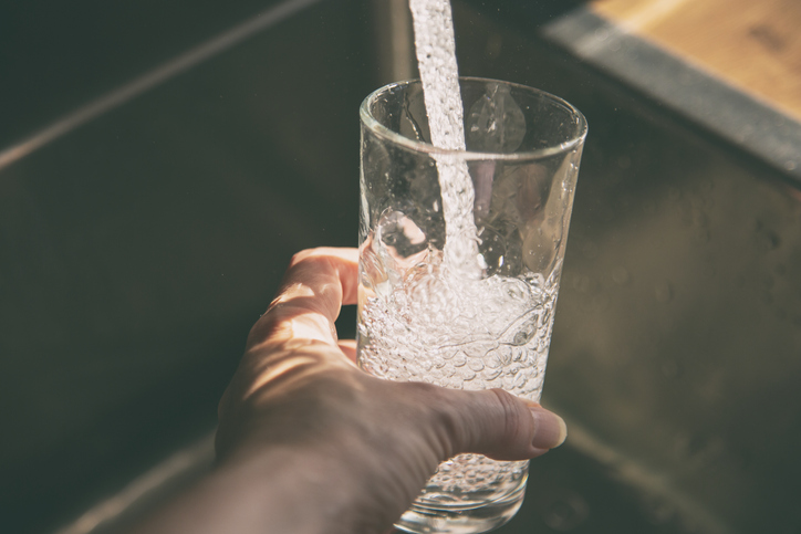 Female pouring fresh drinking tap water into the glass. Close-up on hand holding glass.